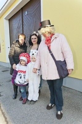 Eine Gruppe von Menschen in Kostümen, darunter eine Frau in einer rosa Jacke und ein Kind in einem weißen Bärenkostüm, stehen vor einem gelben Gebäude.