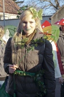 Eine Frau in einer Feen-Verkleidung mit grünen Blättern und Flügeln steht im Freien und lächelt in die Kamera.