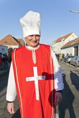 Ein Mann in einem roten und weißen Gewand mit einer weißen Mitra und einem Kreuz auf der Brust steht auf der Straße.