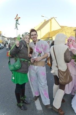 Drei Menschen in Kostümen posieren für ein Foto auf einer Straße mit Gebäuden im Hintergrund.