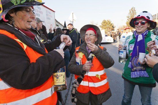 Eine Gruppe von Menschen in orangenen Westen und Hüten steht auf einer Straße, eine Frau trinkt aus einer Flasche, während eine andere etwas in einen Becher gießt.