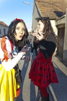 Zwei Frauen in Kostümen, eine in einem bunten Kleid und die andere in einem roten Kleid mit Punkten, stehen auf einer Straße und posieren möglicherweise für ein Foto.