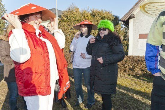 Eine Gruppe von Menschen in Kostümen, darunter eine Frau in einem roten Pilzhut, steht an einem sonnigen Tag im Freien.