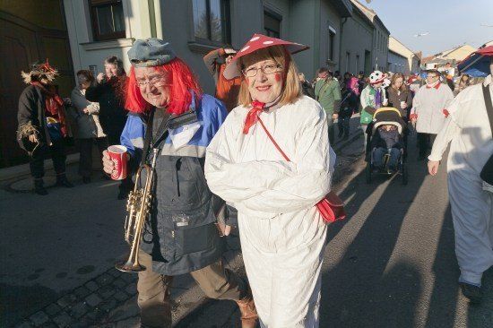 Eine Gruppe von Menschen in Kostümen geht während eines Umzugs eine Straße entlang, wobei einer der Männer eine Trompete und einen roten Becher hält.