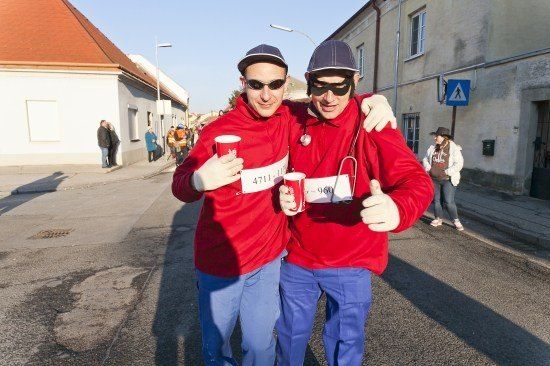 Zwei Männer in roten und blauen Kostümen gehen die Straße entlang, einer hält einen Becher und der andere gibt einen Daumen hoch.