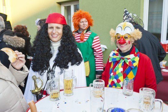 Eine Gruppe von Menschen in Kostümen, darunter ein Pirat, ein Clown und ein Clown mit roter Nase, sitzen um einen Tisch mit Biergläsern.