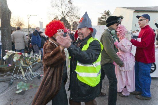 Eine Gruppe von Menschen in Kostümen, darunter ein Mann in einer Warnweste, steht auf einer Straße. Ein Mann trägt eine rote Perücke und eine Brille.