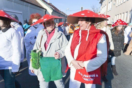Eine Gruppe von Menschen in Pilzkostümen zieht bei einem Umzug. Eine Frau hält eine grüne Tasche und eine andere hat eine rote Tasche mit den Worten 'Alles, was du brauchst, ist Liebe'.