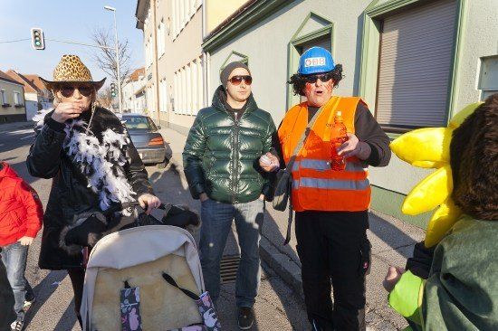 Eine Gruppe von Menschen in Kostümen auf einer Stadtstraße, einer hält einen Kinderwagen.