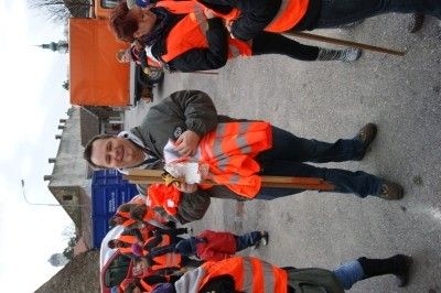 Eine Gruppe von Menschen in orangefarbenen Sicherheitswesten steht auf der Straße. Ein Mann hält einen Stock und lächelt.
