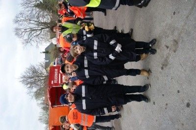 Eine Gruppe von Personen in Sicherheitsausrüstung, darunter Kinder, steht in einer Reihe neben einem roten Feuerwehrwagen.