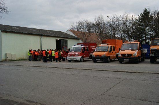 Eine Gruppe von Personen in Sicherheitswesten steht in der Nähe eines Gebäudes, vor dem Notfallfahrzeuge geparkt sind.