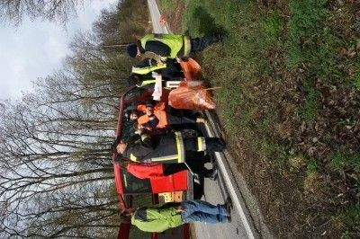 Eine Gruppe von Personen in Sicherheitsausrüstung steht neben einem roten Fahrzeug am Straßenrand, möglicherweise bei einem Vorfall.