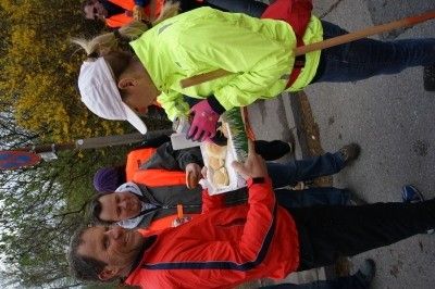 Eine Gruppe von Menschen in reflektierenden Kleidungsstücken und Hüten steht auf einer Straße, wobei eine Person einen Teller mit Essen hält.