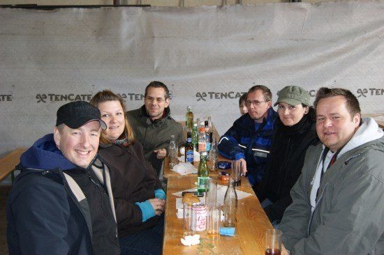 Eine Gruppe von Menschen sitzt um einen Tisch mit Flaschen und Gläsern und lächelt für ein Foto.