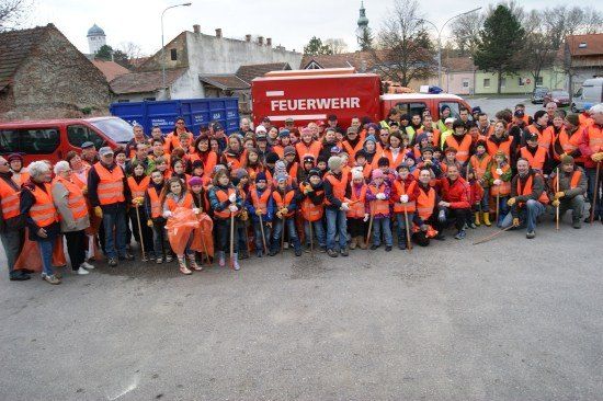 Eine große Gruppe von Menschen in orangenen Westen, einige halten Besen, posiert für ein Foto vor einem roten Feuerwehrauto.