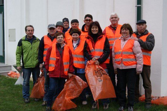 Eine Gruppe von Freiwilligen in orangefarbenen Westen und mit orangefarbenen Tüten stehen vor einem weißen Gebäude.
