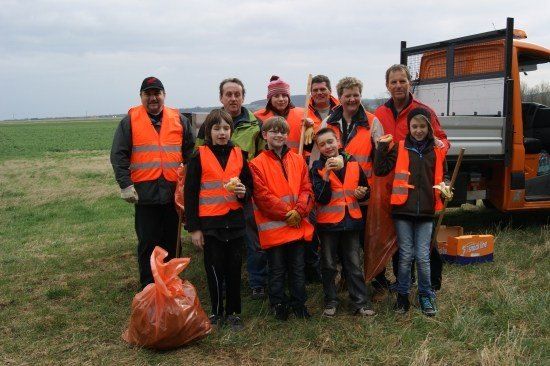 Eine Gruppe von Menschen in orangefarbenen Westen steht auf einem Feld, lächelt und hält Essen. Sie stehen vor einem Lastwagen.