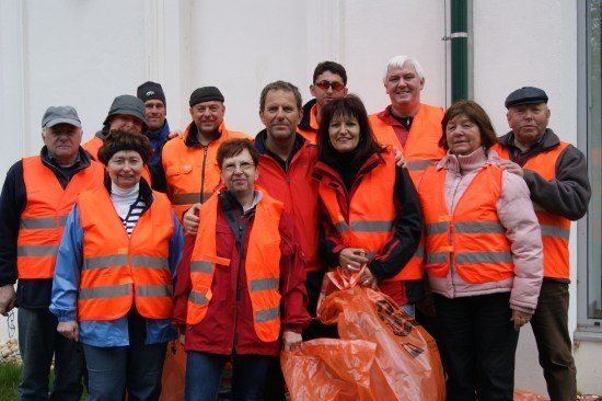 Eine Gruppe von Menschen in orangenen Sicherheitswesten und Jacken posiert für ein Foto vor einem Gebäude.