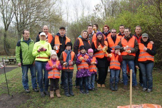 Eine Gruppe von Erwachsenen und Kindern in orangenen Westen posiert für ein Foto im Park und hält Essen in den Händen.