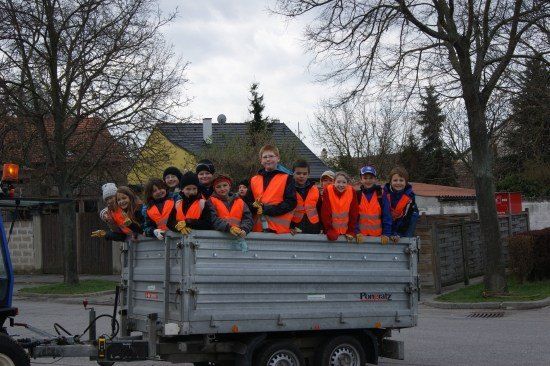 Eine Gruppe von Kindern in orangefarbenen Westen fährt in einem Anhänger auf einer Straße.