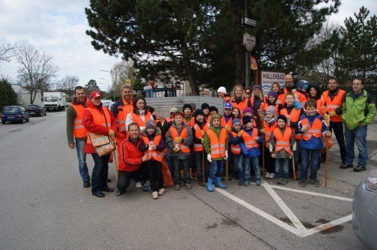Eine Gruppe von Menschen, einschließlich Kindern, die orange Westen tragen und Stöcke halten, posiert für ein Foto am Straßenrand.