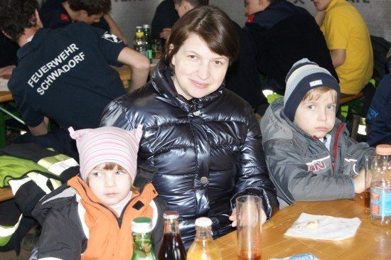 Eine Frau und zwei Kinder sitzen an einem Tisch in einem überfüllten Restaurant, mit einem Feuerwehrmann im Hintergrund.
