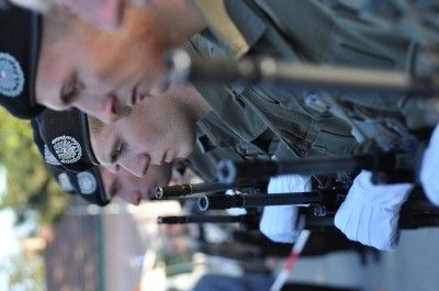 Eine Gruppe von Soldaten in Uniform, mit Mützen, steht in einer Reihe mit Gewehren, möglicherweise an einer militärischen Zeremonie teilnehmend.