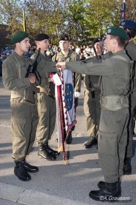 Eine Gruppe von Soldaten in Uniform überreicht einem Mann vor ihnen eine Flagge.