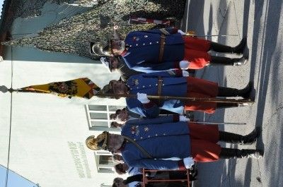 Eine Gruppe von Männern in blauen und roten Uniformen steht vor einem Gebäude und hält Fahnen und Stöcke.
