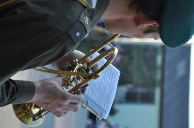 Ein Soldat in einem grünen Hut und Uniform spielt Trompete und schaut auf Noten.