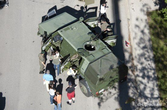 Eine Luftaufnahme eines Militärfahrzeugs, um das sich Menschen an einem sonnigen Tag versammelt haben.