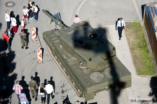 Eine Vogelperspektive eines Militärpanzers mit umstehenden Personen. Ein Mann in Anzug geht auf dem Bürgersteig.