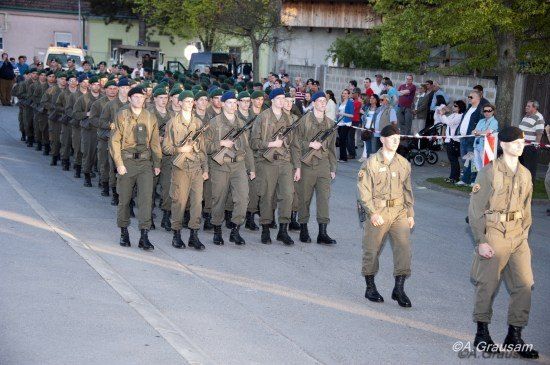 Eine Reihe von Soldaten in Uniform marschiert die Straße hinunter, mit Zuschauern an der Seite.