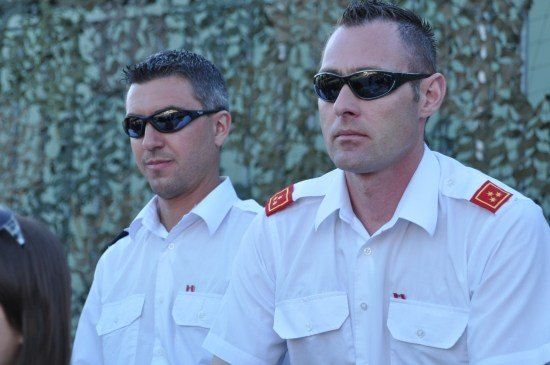 Zwei Männer in weißen Uniformen mit roten Aufnähern auf den Schultern stehen nebeneinander, beide tragen Sonnenbrillen.