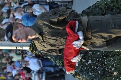 Ein Soldat in Uniform hält ein rotes Tuch, möglicherweise eine Flagge, vor einer Menge.