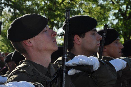 Eine Gruppe von Soldaten in Uniform, mit schwarzen Baretten und weißen Handschuhen, steht in Formation und hält Gewehre.
