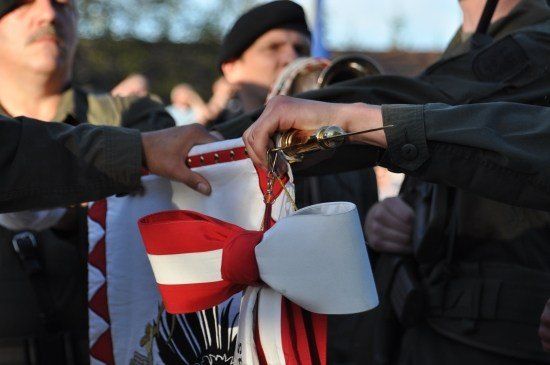 Soldaten in Uniform halten eine Flagge mit einem roten und weißen Bogen und bereiten sich auf eine Zeremonie vor.