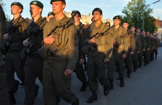 Eine Reihe von Soldaten in Uniform marschiert mit Gewehren auf einer Straße.