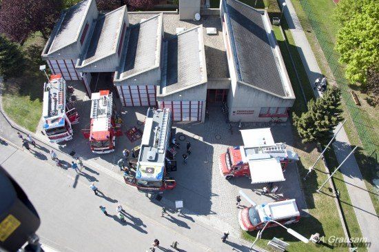 Ein Luftbild einer Feuerwache mit mehreren Feuerwehrfahrzeugen, die draußen geparkt sind, und Menschen, die herumlaufen.
