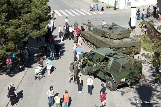 Eine Luftaufnahme einer Straße, auf der sich Menschen um Militärfahrzeuge versammelt haben, darunter ein Panzer und ein gepanzertes Auto.