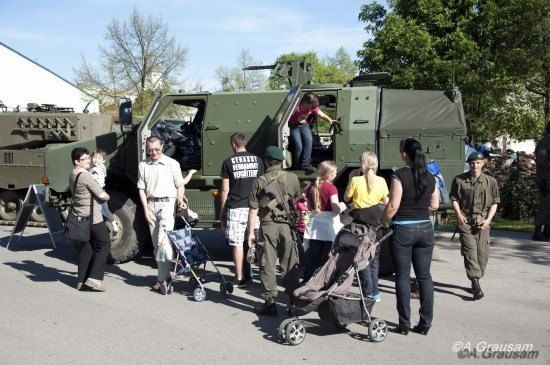 Eine Gruppe von Menschen, einschließlich Kindern, versammelt sich um ein Militärfahrzeug. Eine Frau klettert in das Fahrzeug, während andere zusehen.