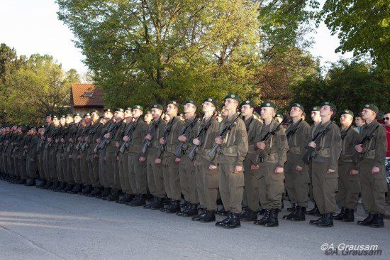 Eine Reihe von Soldaten in Uniform, Gewehre haltend, in Formation stehend mit Bäumen und einem Haus im Hintergrund.