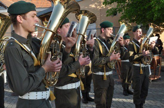 Eine Militärkapelle von Männern in grünen Uniformen spielt Blechblasinstrumente an einem sonnigen Tag.