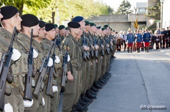 Eine Reihe von Soldaten in Militäruniformen steht in Formation, Gewehre in der Hand, mit Zuschauern hinter einer Barriere im Hintergrund.