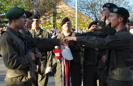 Eine Gruppe von Militärangehörigen in Uniform nimmt an einer Zeremonie teil, bei der eine Person eine Flagge an eine andere übergibt.