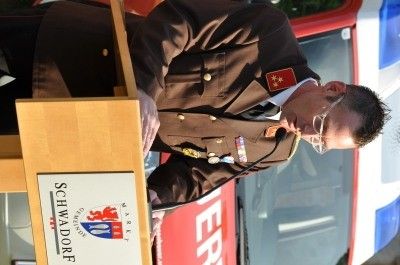 Ein Mann in Uniform hält eine Rede an einem Rednerpult mit Mikrofon vor einem Rettungsfahrzeug.