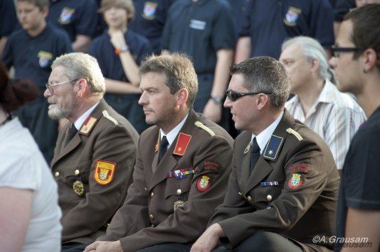 Drei Männer in Militäruniformen sitzen zusammen in einer Menschenmenge, einer trägt eine Brille und der andere eine Sonnenbrille.