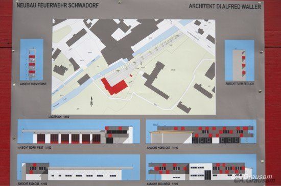 Ein Schild zeigt architektonische Pläne für das Neubau Feuerwehr Schwadorf, entworfen von Alfred Waller. Es enthält einen Lageplan und vier perspektivische Ansichten des Gebäudes.