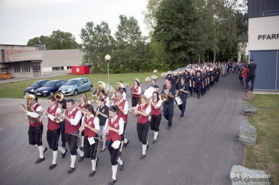 Eine Blaskapelle in roten und weißen Westen und schwarzen Hosen spielt Instrumente, während sie eine Straße entlanggeht.